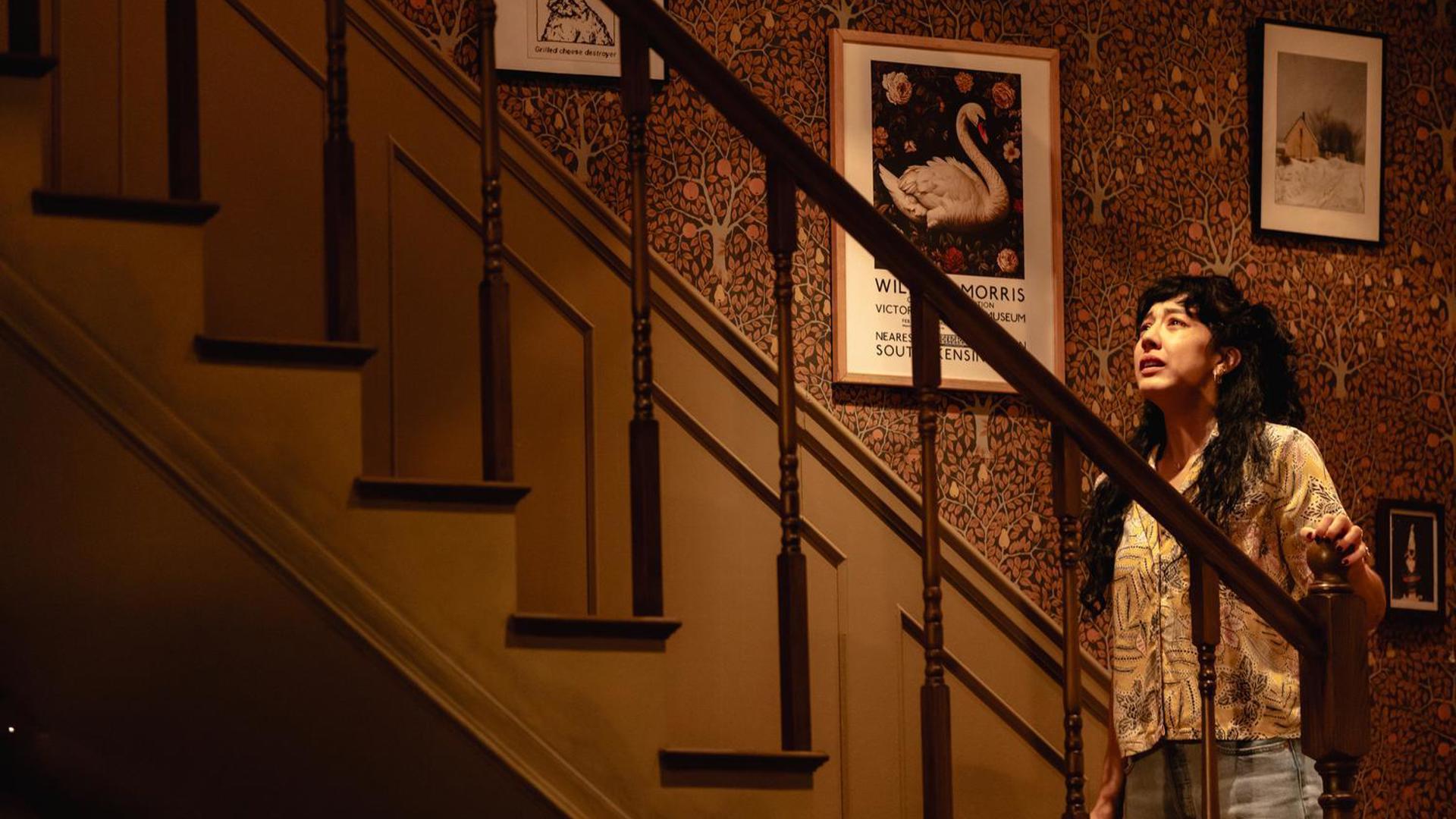 A distraught woman looking up the staircase.