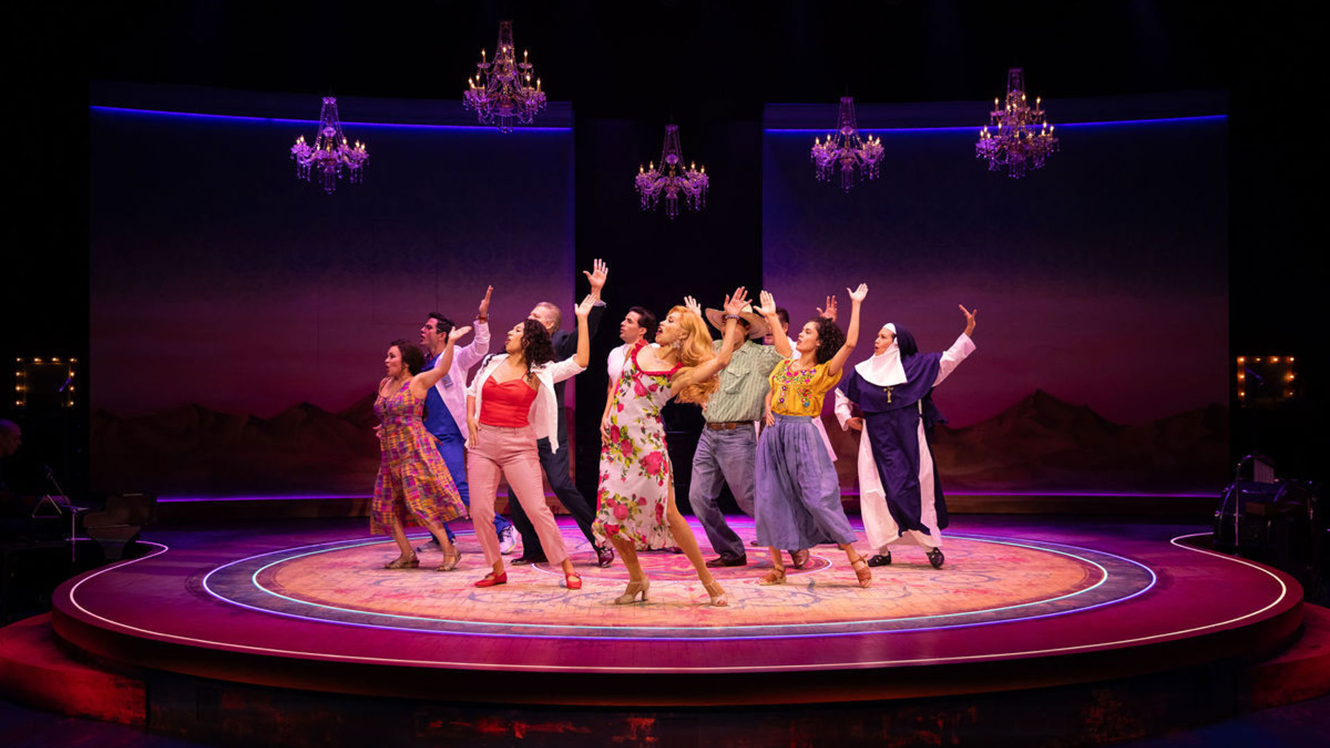 A group of actors stand onstage, holding their right hands up while dancing.