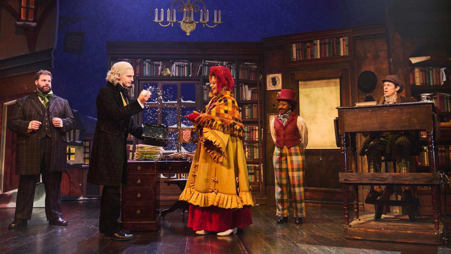 Five performers stand on stage, with one giving the other some snow.