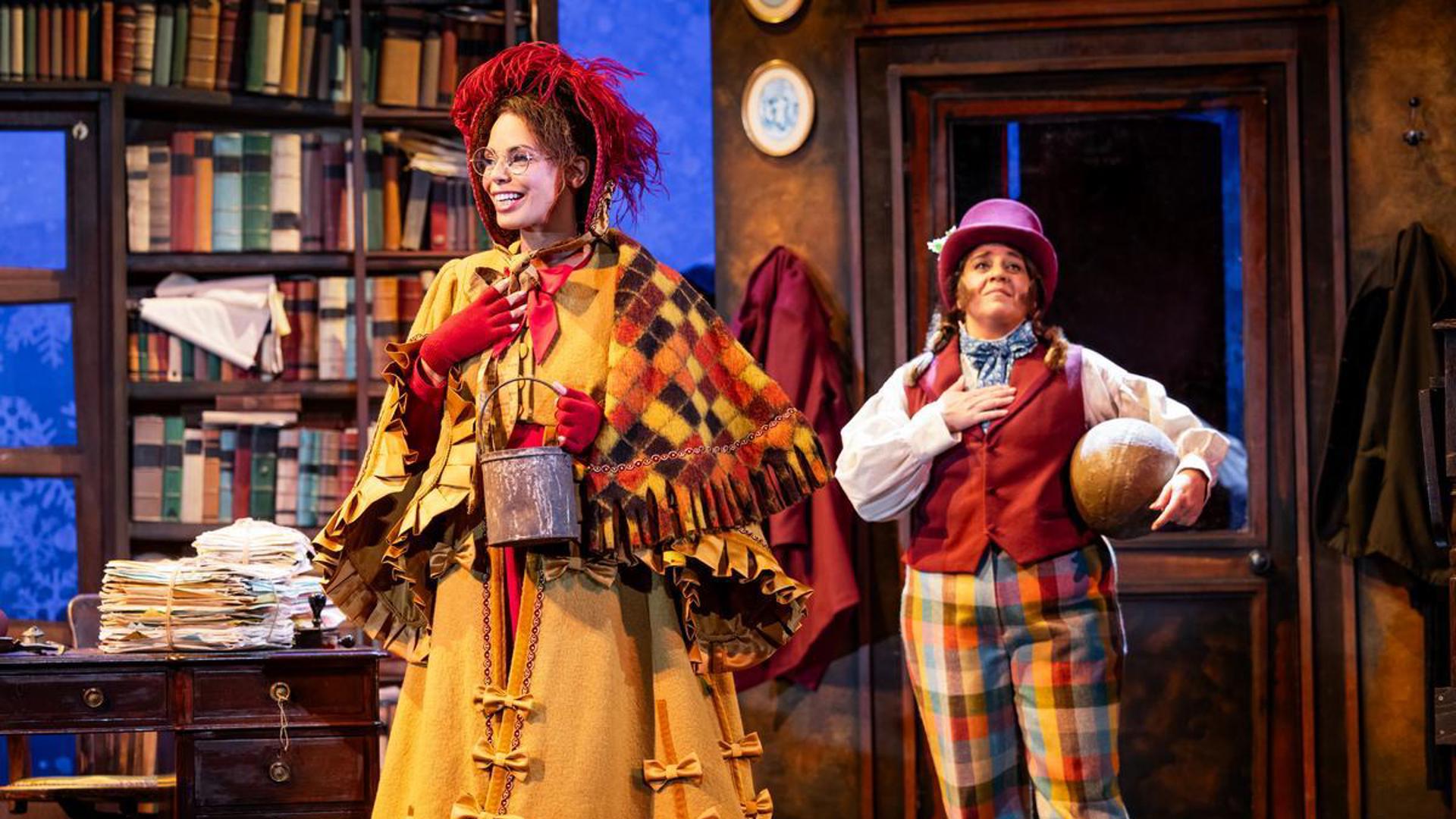 Two performers stand on stage, one holding a can and one holding a basketball with their right hands on their chests.