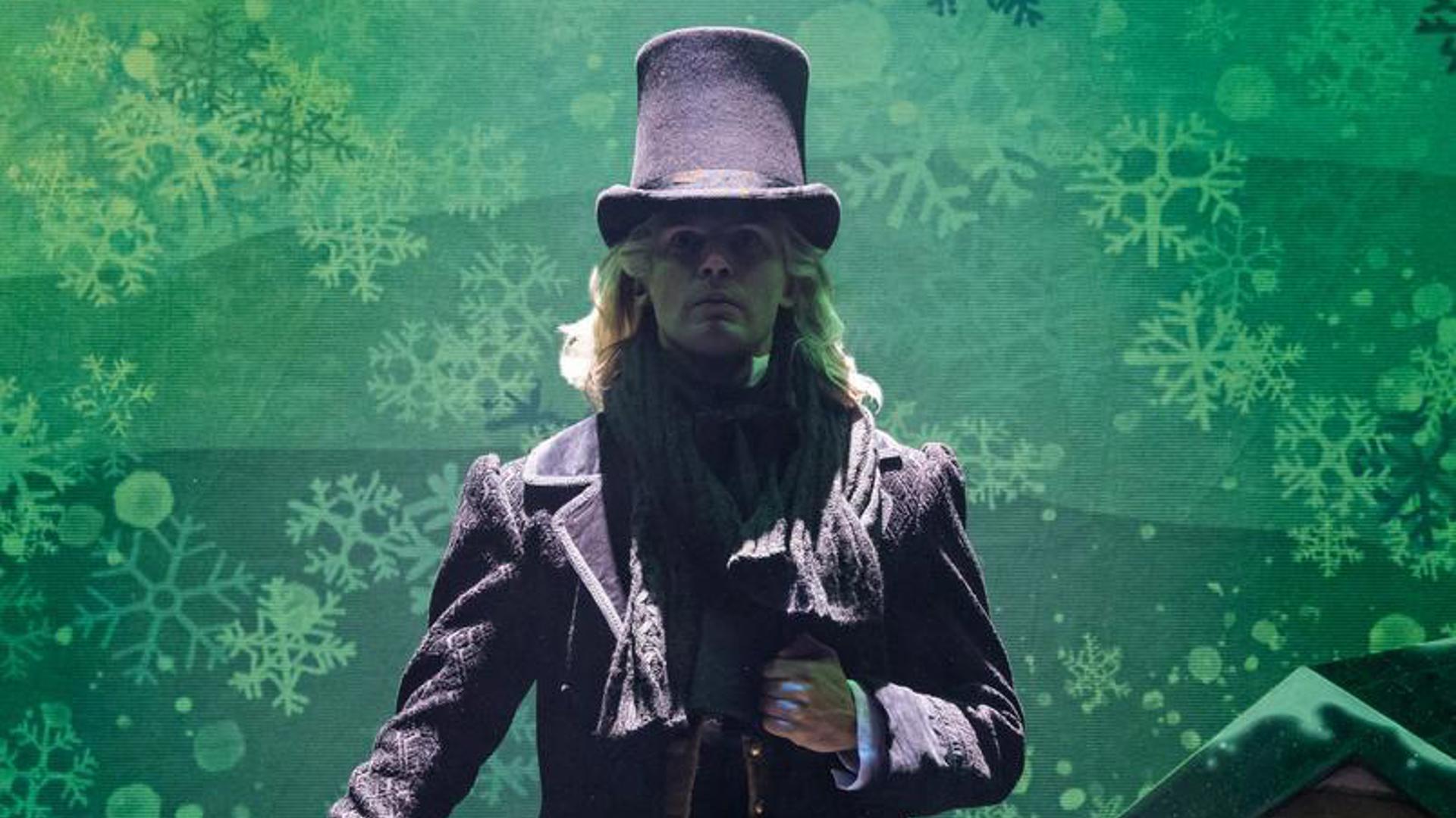 A performer stands on stage with a top hat and a cane looking out at the audience.