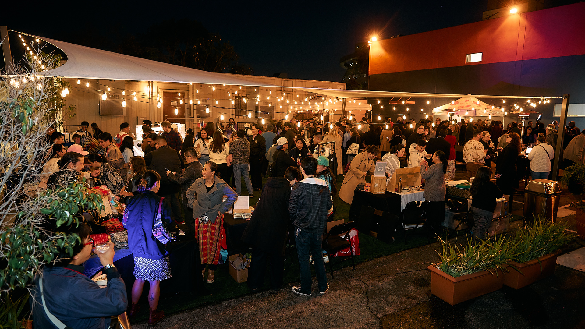 A gathering of excited theatregoers under a canopy and string lights at the Music Center Annex. 