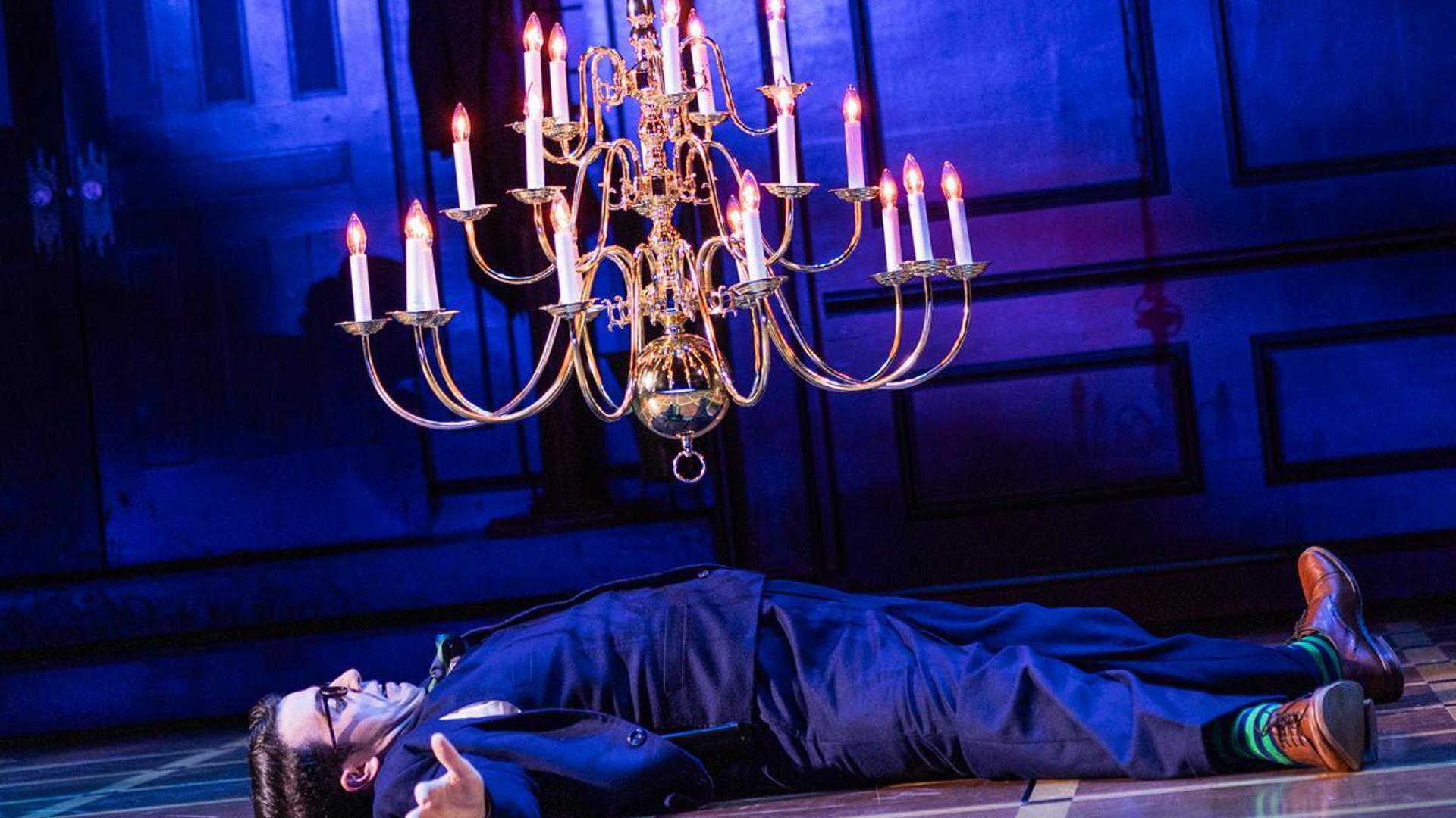 A man is lying spread out on the floor, mouth agape as a falling chandelier hangs over him.