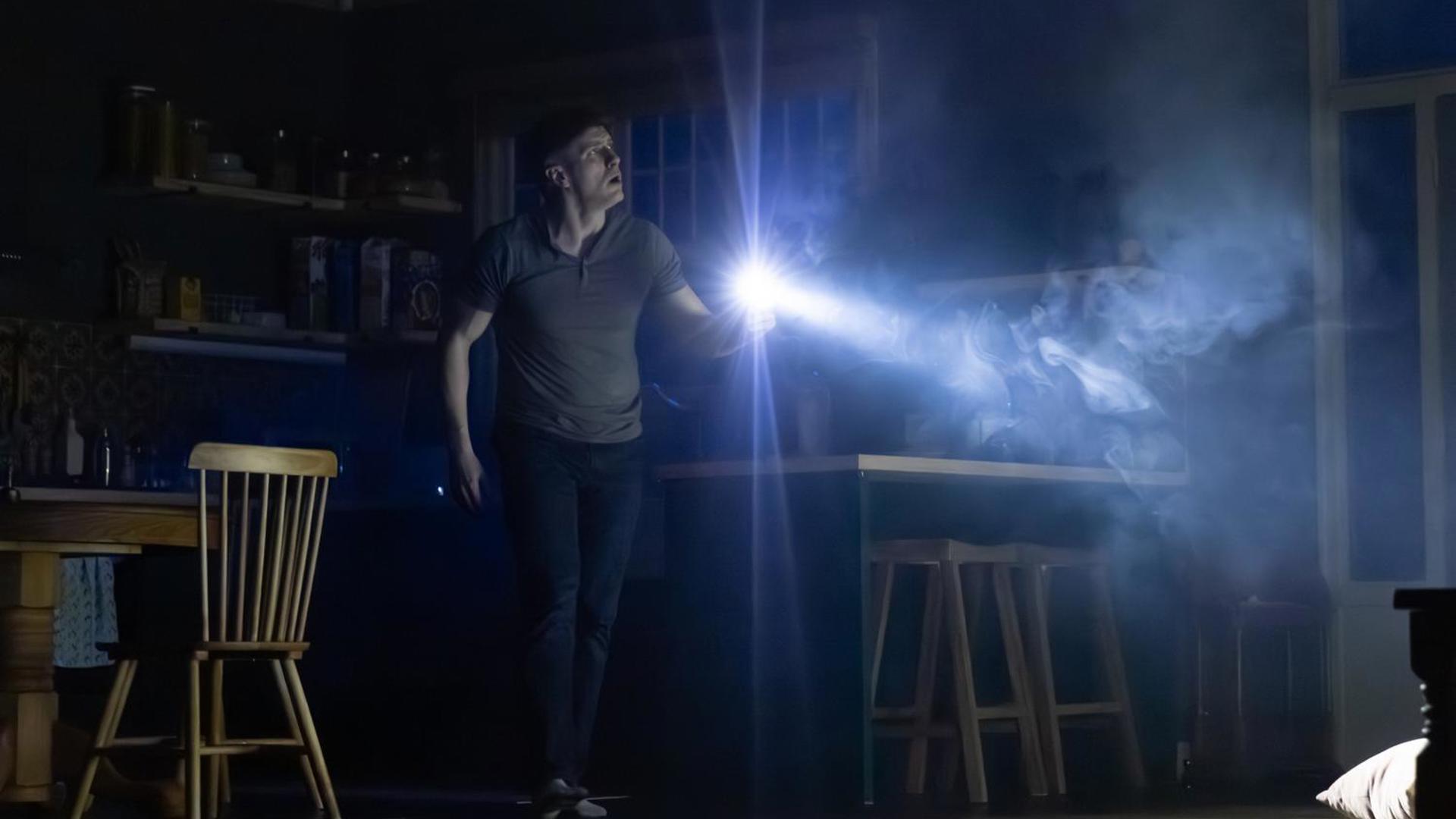 A man in a dark house with a flashlight.