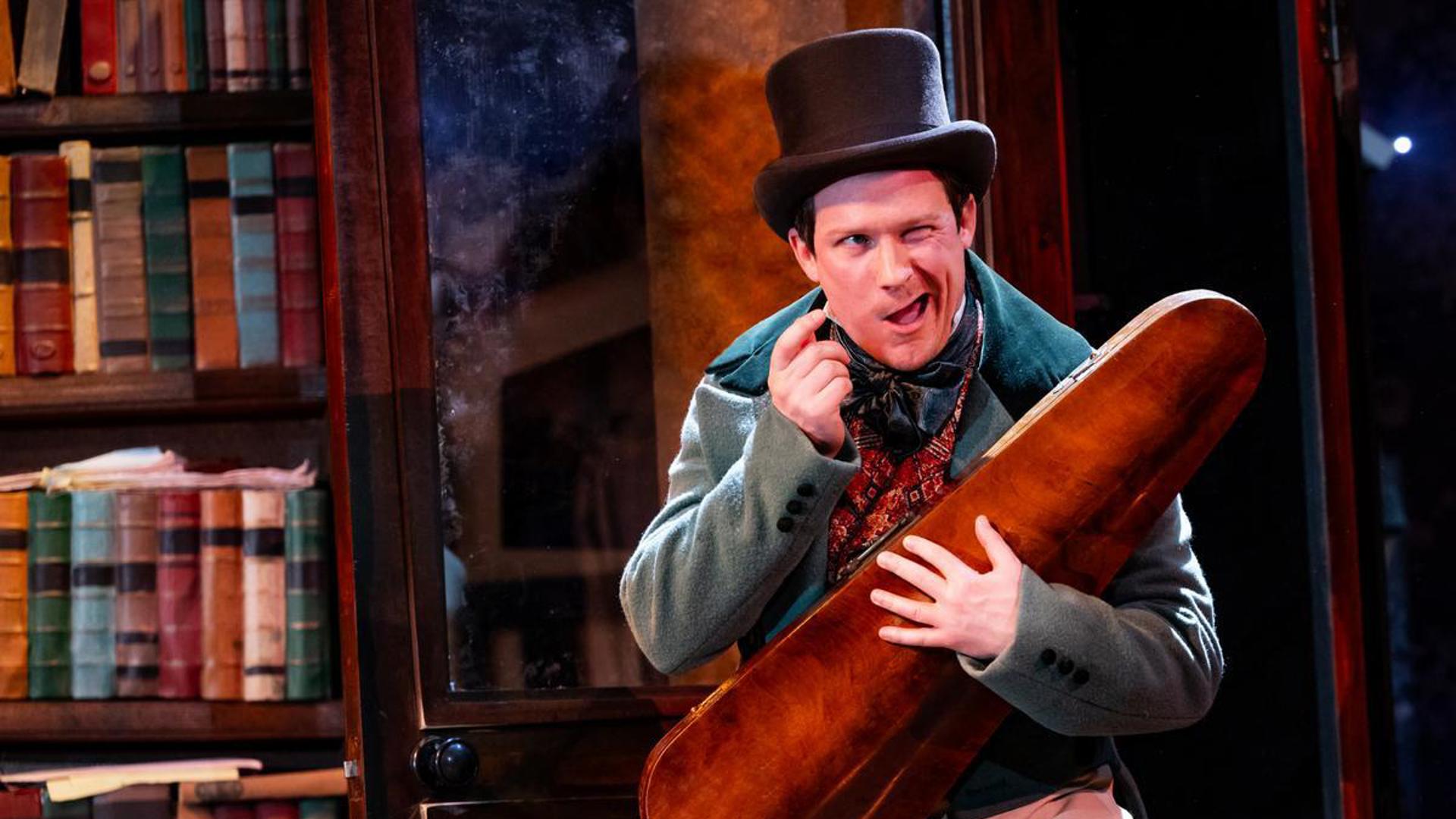 A performer in a top hat holding a string instrument case and winking.